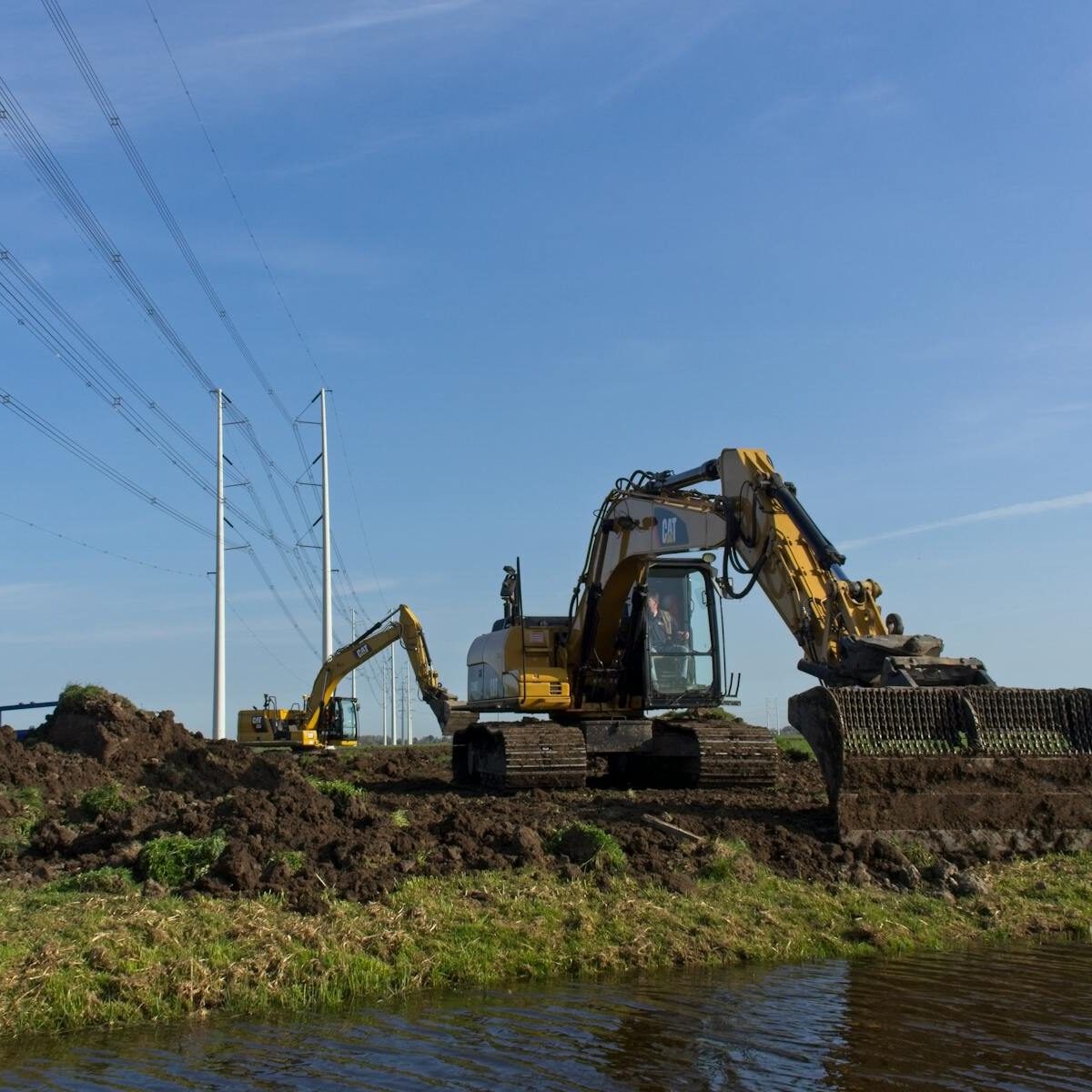 Excavators performing earthmoving tasks near utility poles in Zuid-Holland, Netherlands.