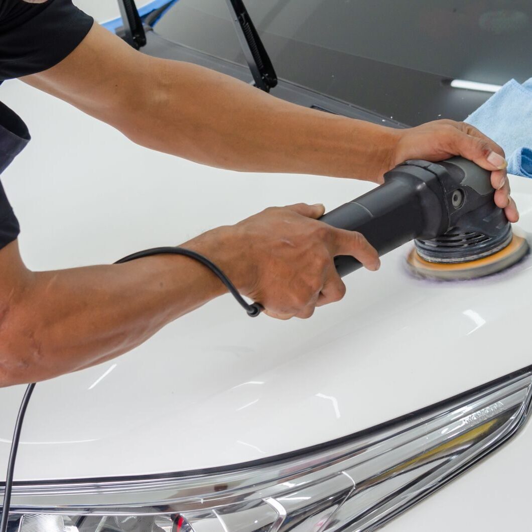 Close-up of a mechanic using a rotary polisher on a white car bonnet for detailing.