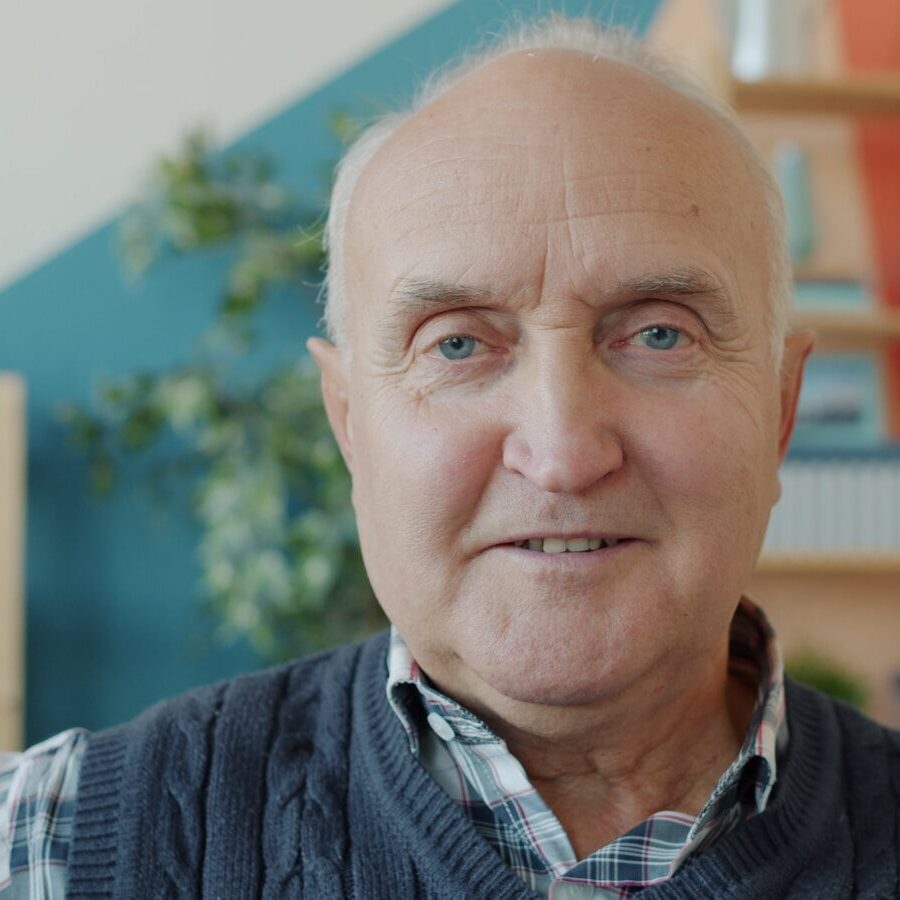 Elderly man with a warm smile in a living room.